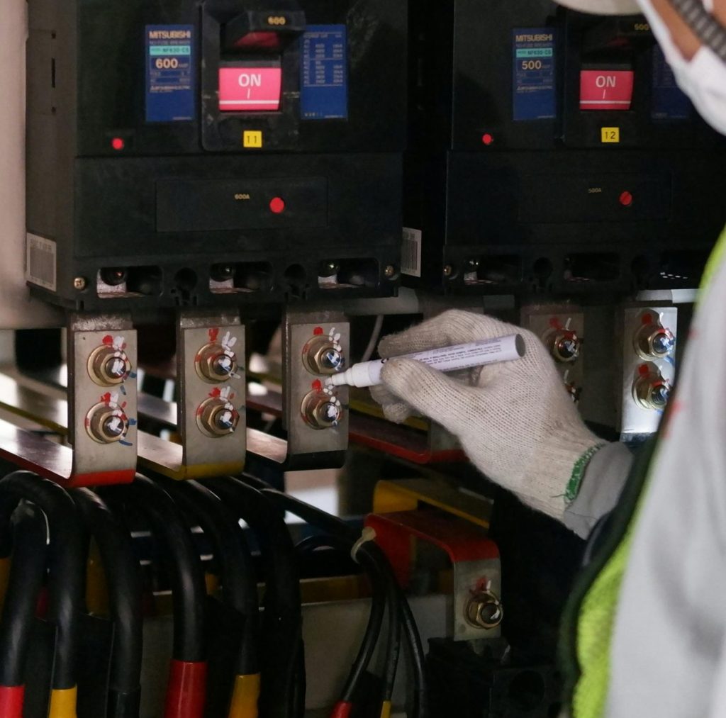 Technician wearing safety gear inspecting electrical panels in an industrial setting.